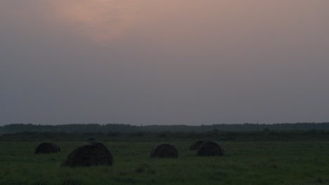 Sunset-wildfire-sky-smog-red-sun-over-countryside-landscape-with-hay-rolls