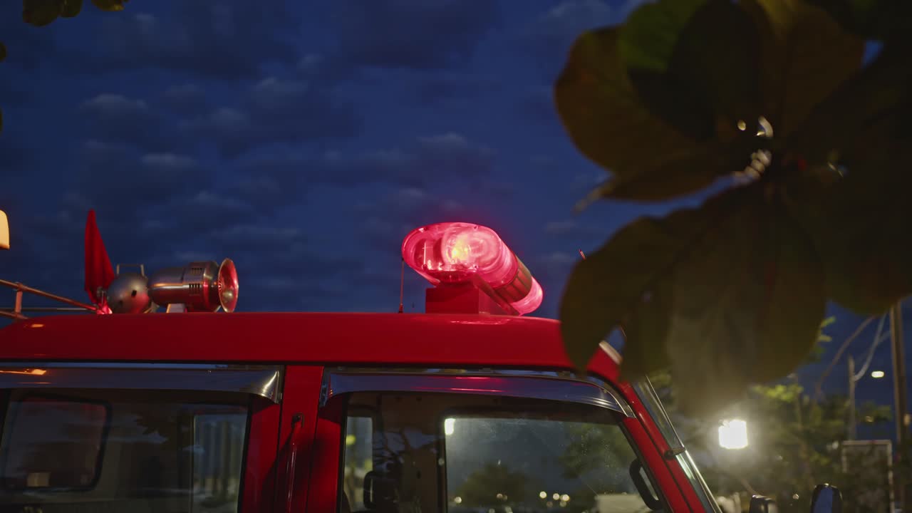 Red firetruck with its emergency siren light illuminated under a dark blue evening sky. Close up slow motion view