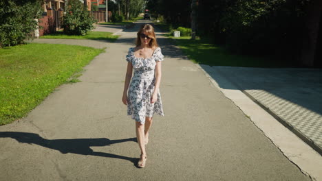 charming woman strolling down residential street in floral dress and sunglasses, walking confidently on sunny day past brick fences and leafy trees, enjoying peaceful neighborhood