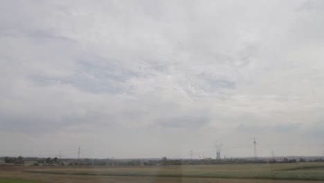 countryside landscape seen from a moving train, capturing fields and a cloudy sky