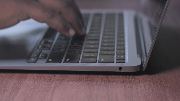 Primo piano di mani che digitano su un laptop argentato.