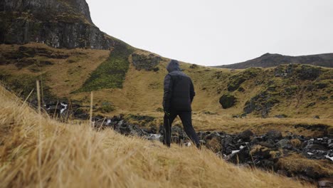 Male-tourist-walk-near-rocky-mountain-river-bed-and-grass-covered-hill