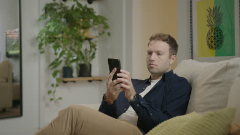 Man-sitting-on-sofa-using-cell-phone-and-social-media-while-relaxing