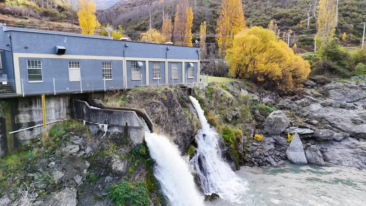 Drone captures a hydroelectric station with cascading waterfalls in Queenstown, New Zealand, surrounded by autumn foliage