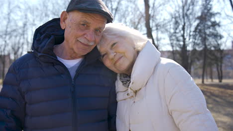 pareja mayor abrazándose y mirando la cámara en el parque en un día de invierno