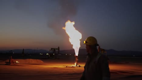 energy extraction at twilight: a worker observes a gas flare's fiery eruption against the evening sky, signifying the power and beauty of resource harvesting