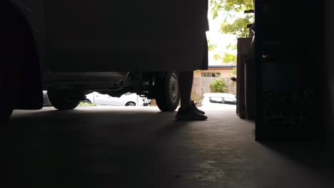 silueta de un hombre que sale de un coche desde el lado de los conductores en vaqueros y entra en la casa en un garaje oscuro iluminado por la luz exterior