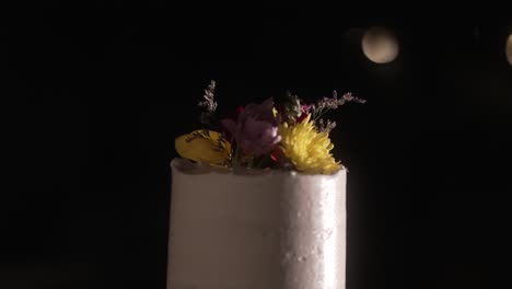 two tier rustic wedding cake with floral toppings lit by romantic evening bokeh lights