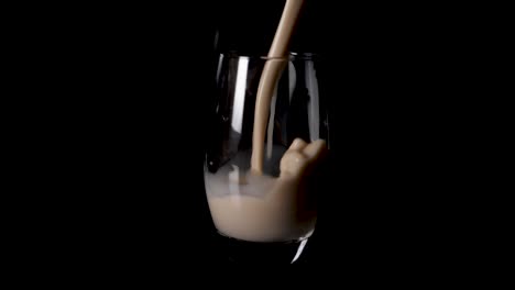 Vegan-hazelnut-milk-being-poured-in-glass,-spills-over-onto-black-surface-table