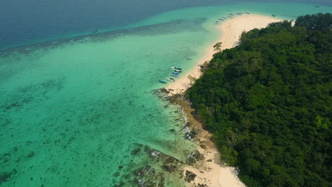 drone de agua turquesa y clara baña una playa blanca rodeada de montaña de piedra caliza en una isla phi phi