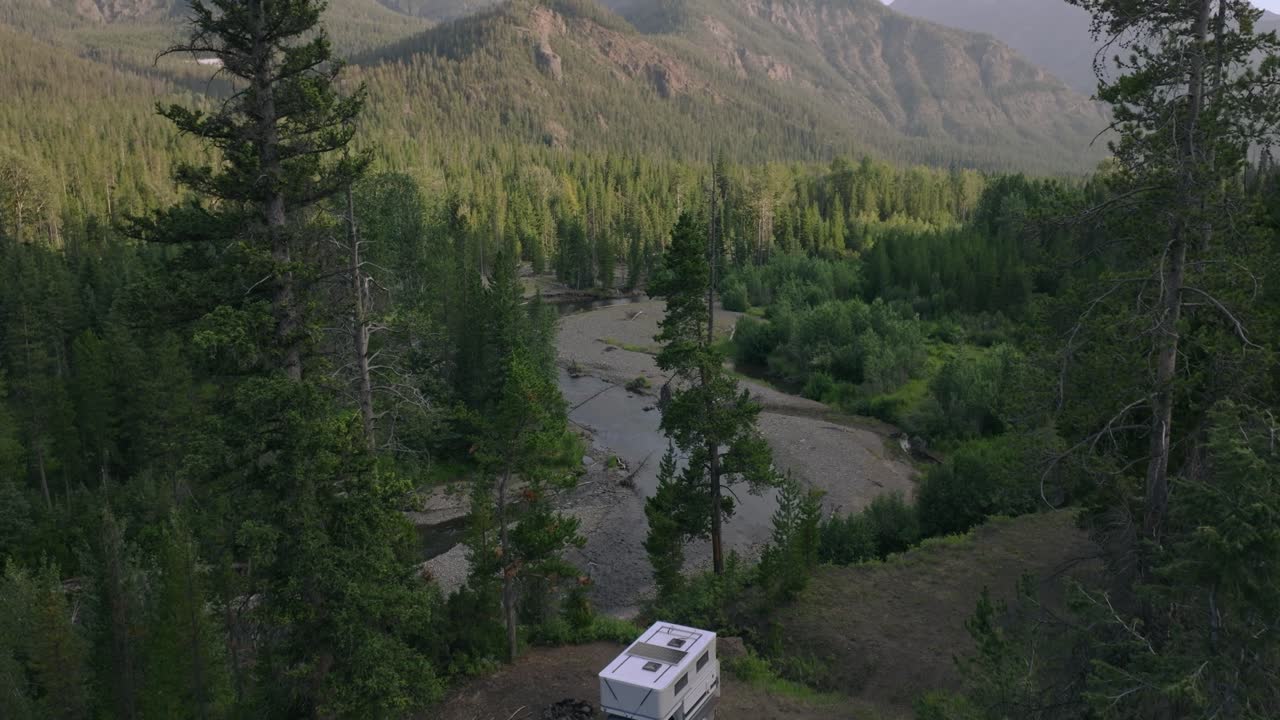 Aerial dolly of a remote camping site in Sunlight Basin, Wyoming, surrounded by dense forest and rugged terrain