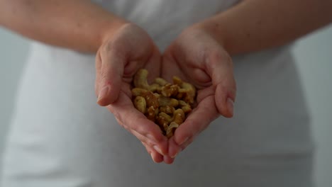 close-up of hands offering walnuts and cashews in late pregnancy session indoors