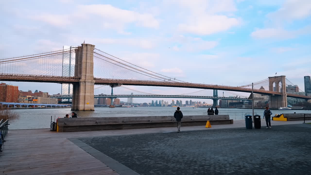 New York, USA, 12 dicembre 2025: Poche persone camminano lungo la banchina di New York, USA. Vista sul Ponte di Brooklyn e sul Ponte di Manhattan sull'East River.