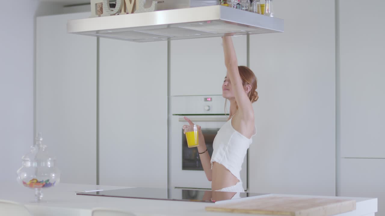 Giovane donna allegra che balla e beve succo di frutta in cucina