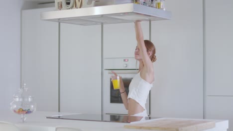 positive young lady dancing and drinking juice in kitchen