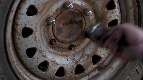 Greasy-hands-of-mechanic-loosen-and-remove-lug-nuts-from-rusty-wheel,-changing-tire