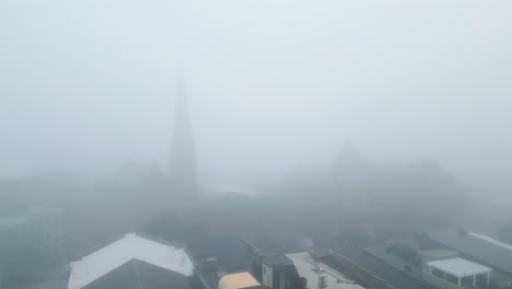 aerial pan tilt down across foggy downtown building scene, thick white mist