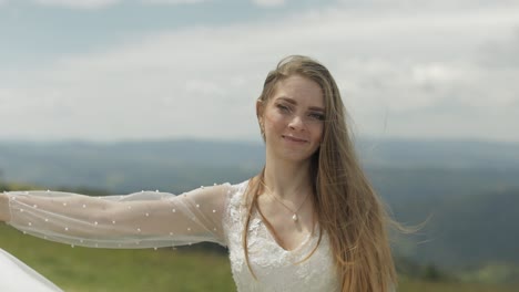 a beautiful bride smiles in her wedding dress while standing in a field with mountains in the background.