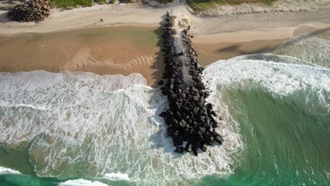 waves breaking on jetty rocks in palm beach, queensland, australia - drone shot