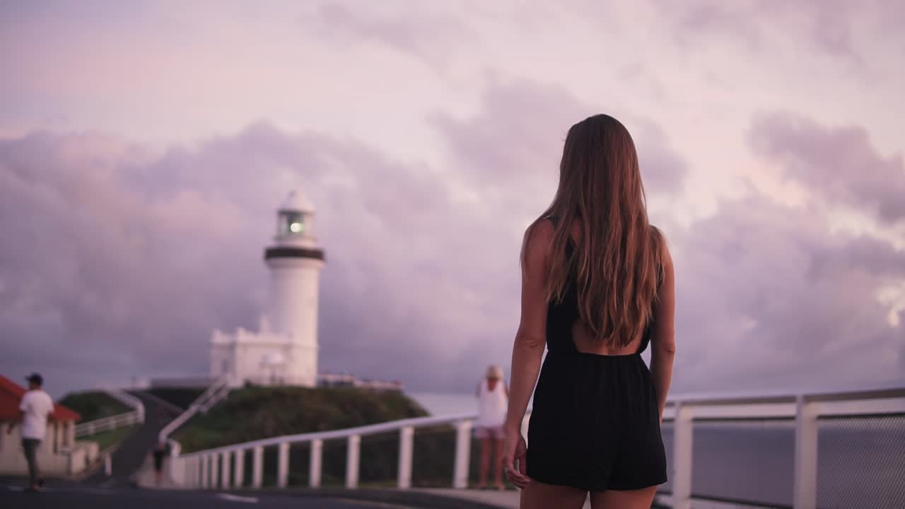 Female walking towards lighthouse in vibrant sunrise