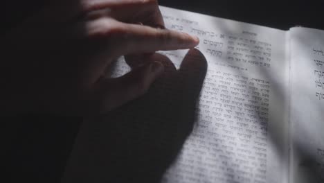 el dedo de la persona señala versos en una biblia hebrea abierta o tanakh con rayas de luz solar