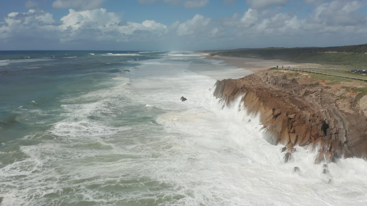 Aerial of white water waves from sea slamming into rocky cliffs