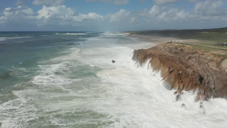 aerial of white water waves from sea slamming into rocky cliffs