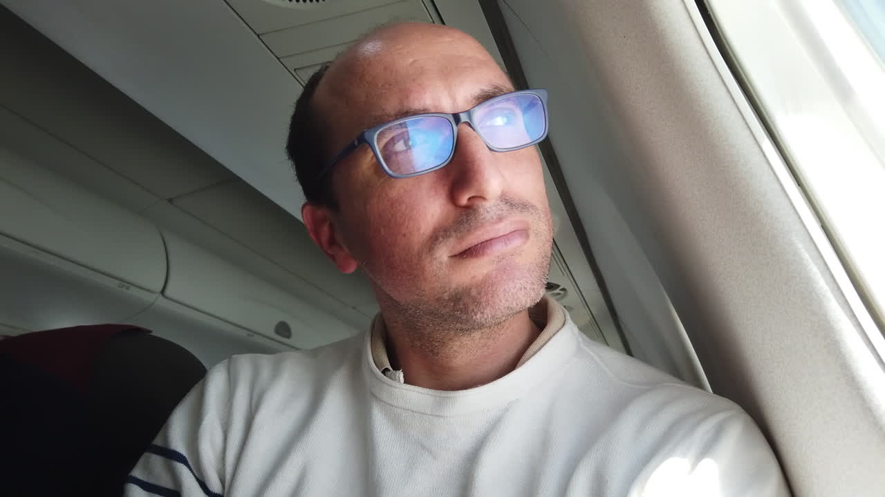 un hombre serio con gafas mira por la ventana de un avión