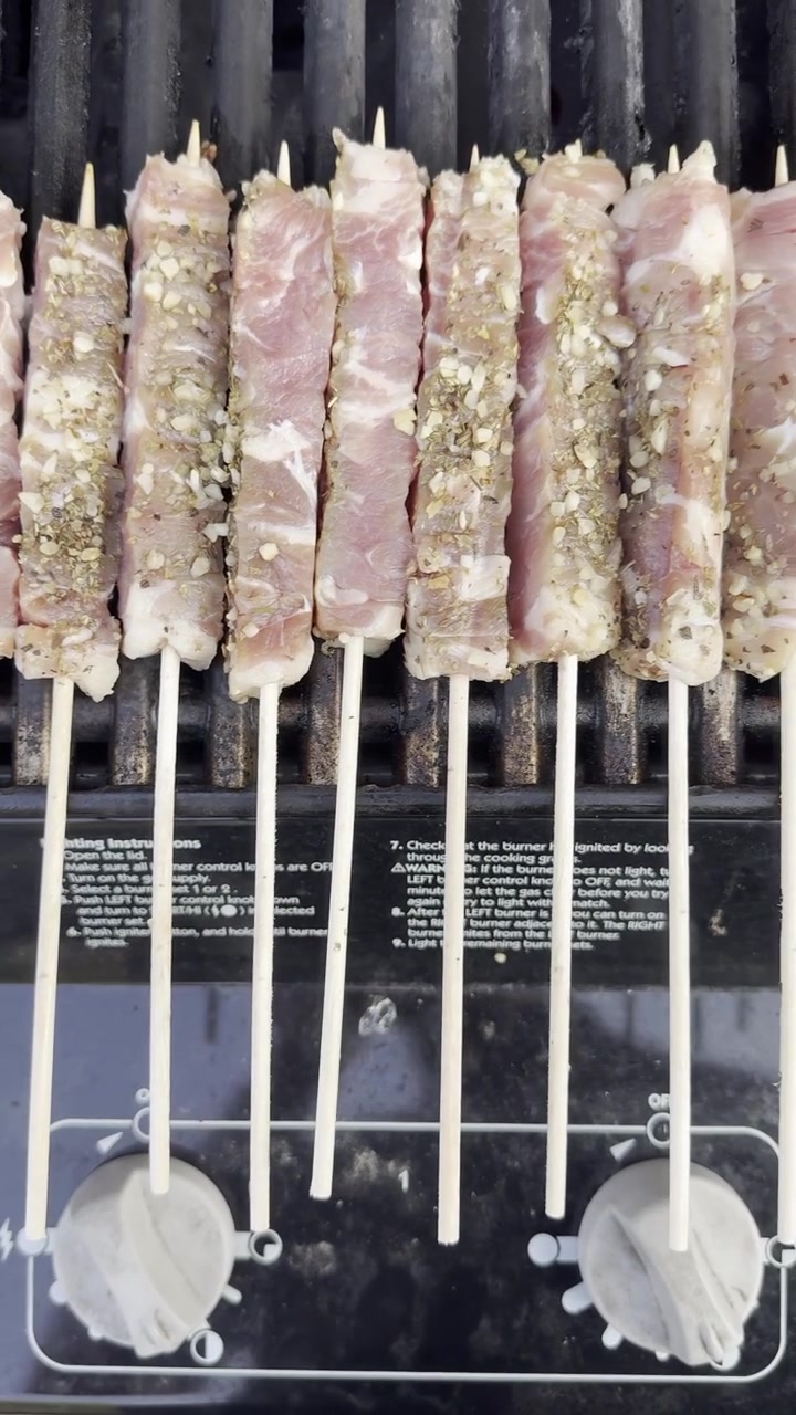 Primo piano di spiedini di souvlaki crudi che cuociono su una griglia barbecue nera con carne fresca sul fuoco.