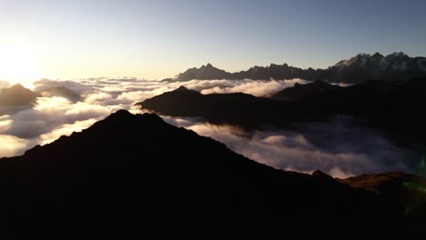 early morning light casts a golden glow over rugged mountain peaks, revealing a stunning view of clouds rolling through the valley below. the serene atmosphere enhances nature's beauty.