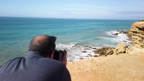 El-Hombre-Toma-Una-Foto-O-Un-Video-De-Una-Gaviota-Volando-Sobre-Una-Cala-Rocosa,-A-Cámara-Lenta