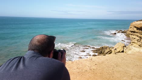 el hombre toma una foto o un video de una gaviota volando sobre una cala rocosa, a cámara lenta