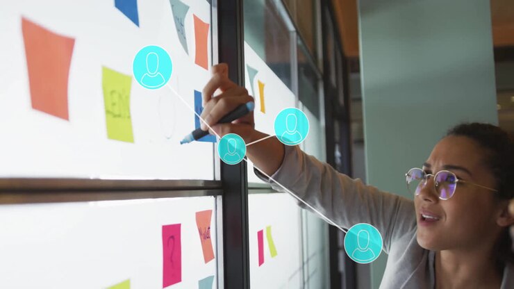 Person skriver på glasvæg med animation af forbundne brugerikoner over post-it-noter