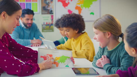 elementary school students with digital tablet looking at map in classroom geography lesson