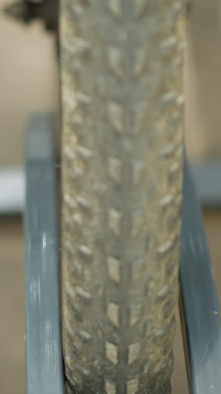 vista frontal en primer plano de un neumático de bicicleta asegurado en un soporte de bicicleta de metal, destacando el marco y los detalles de los radios contra el pavimento de alquitrán de carbón con sombras suaves proyectadas sobre el hormigón