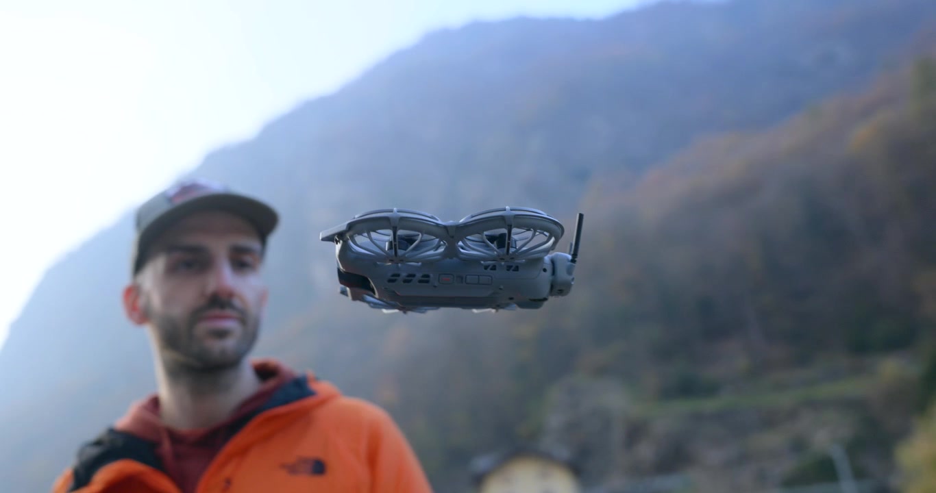 Un uomo afferra un drone compatto che atterra sulla sua mano in una valle di montagna. Scatto ravvicinato all'aperto con un morbido sfondo alpino.