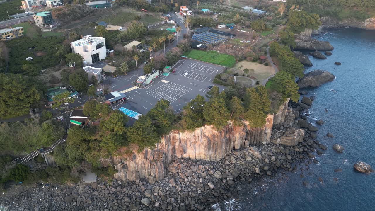 Drone aerial view in South Korea near a cliff with green trees over rocky area parking lot jeju island