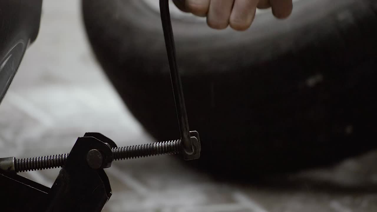 Young man turning a handle of a car jack lifting it right up on the backyard pavement on a cold snowy day, CLOSEUP