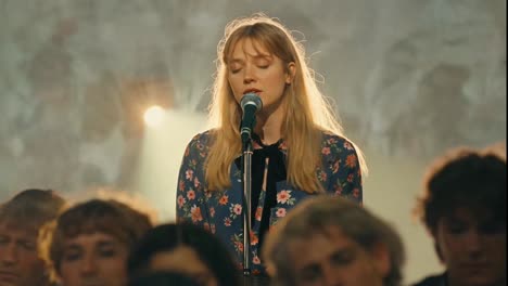 emotional young woman singing into a microphone on a hazy stage.
