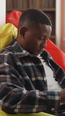 young man reads book sitting on bean bag. reader nestled in cushioned chair in students library lounge immersed in gripping novella. comfort reading concept