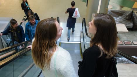 two women talking on an escalator in a shopping mall