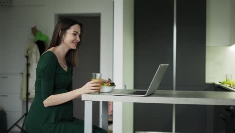 mujer embarazada sentada y comiendo ensalada mientras hace una videollamada en una computadora portátil en casa