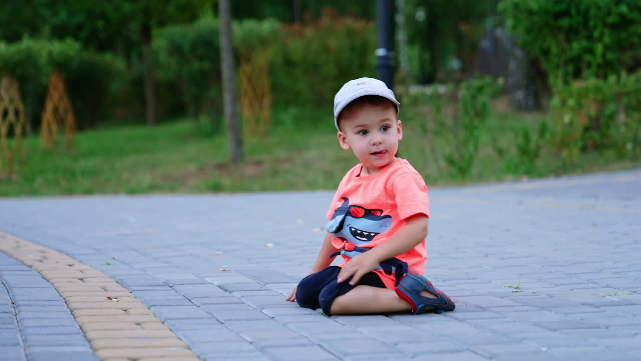Lovely baby boy sitting on his knees on the ground. Cute toddler looks aside with interest.
