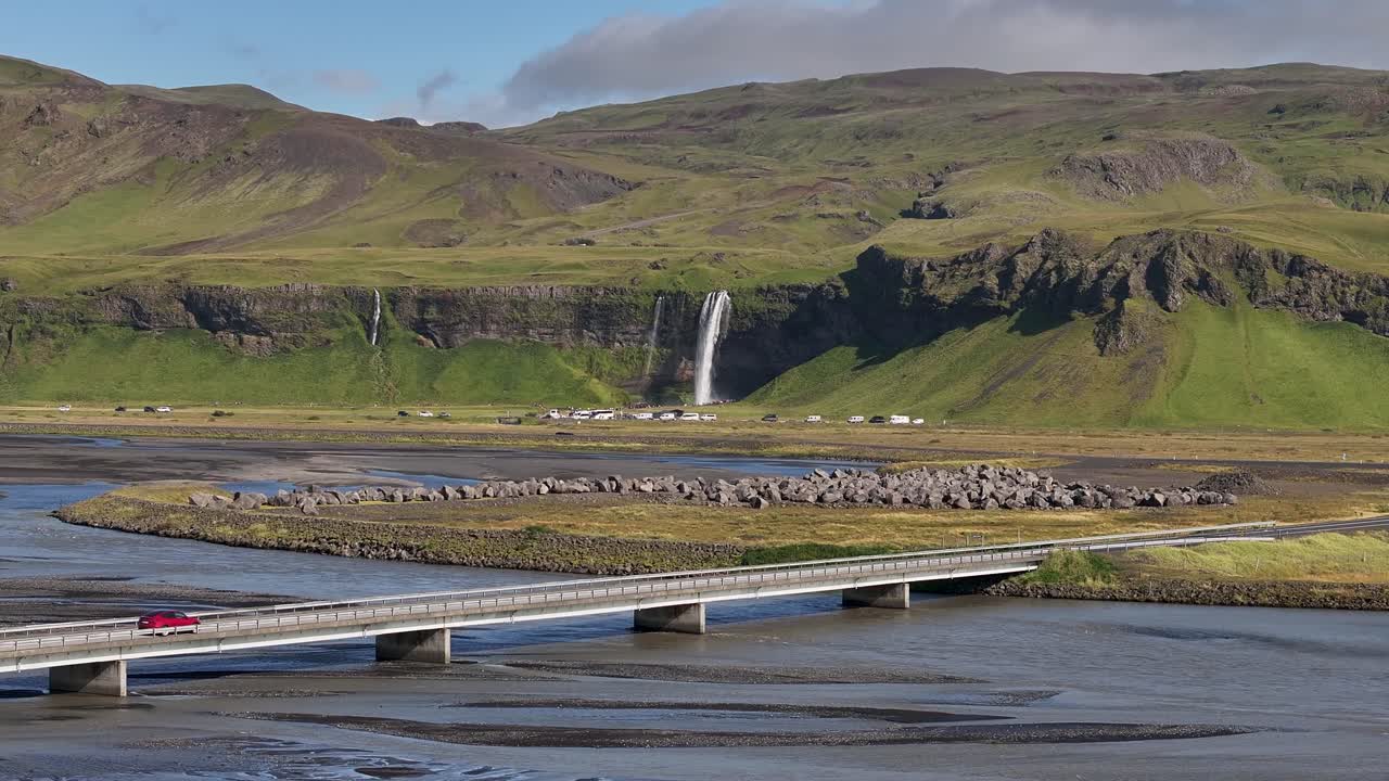 A cinematic view of a distant Seljalandsfoss waterfall in Iceland, showcasing its misty plunge, lush green cliffs, and stunning natural scenery from this iconic South Coast landmark