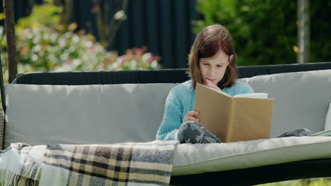 child reading a book, sitting in a garden swing in the backyard of a house