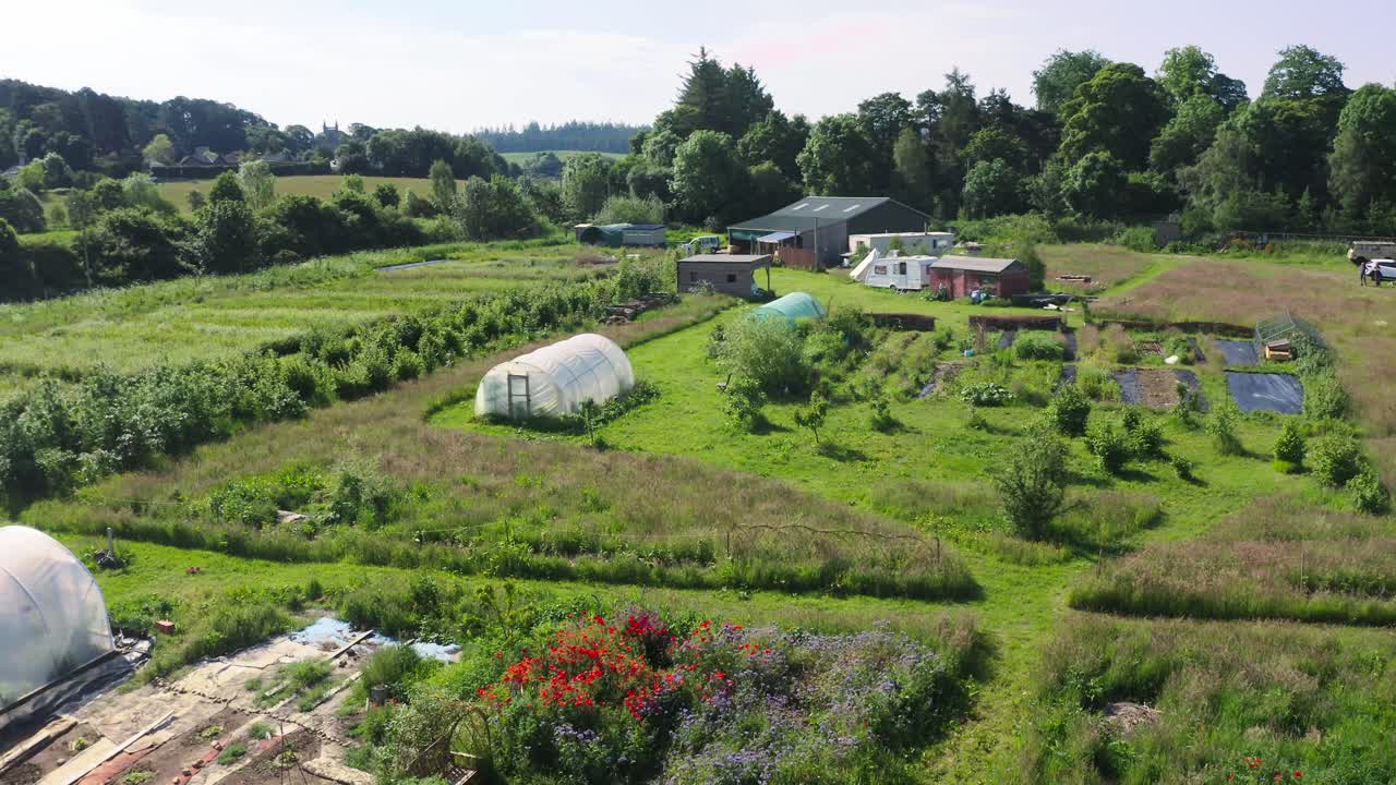 Aerial establishing drone shot of small organic farmland plantation with greenhouses and cultivated crops, ecological sustainable agriculture