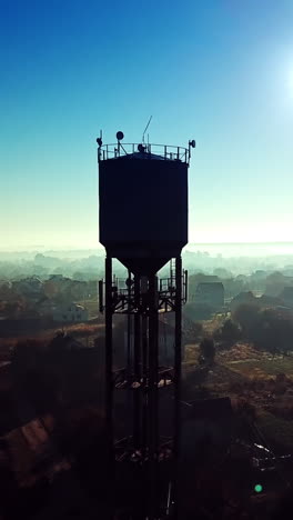 flying over the village near the power station tower on a blue background sunrise. countryside panorama in the morning dawn. aerial view. vertical video