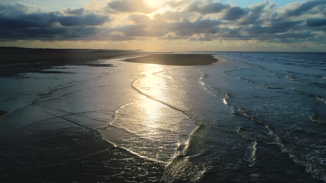 impresionante hermoso drone aéreo bajo disparado sobre pequeñas olas rompiendo en la playa de arena en la hora dorada del atardecer reino unido