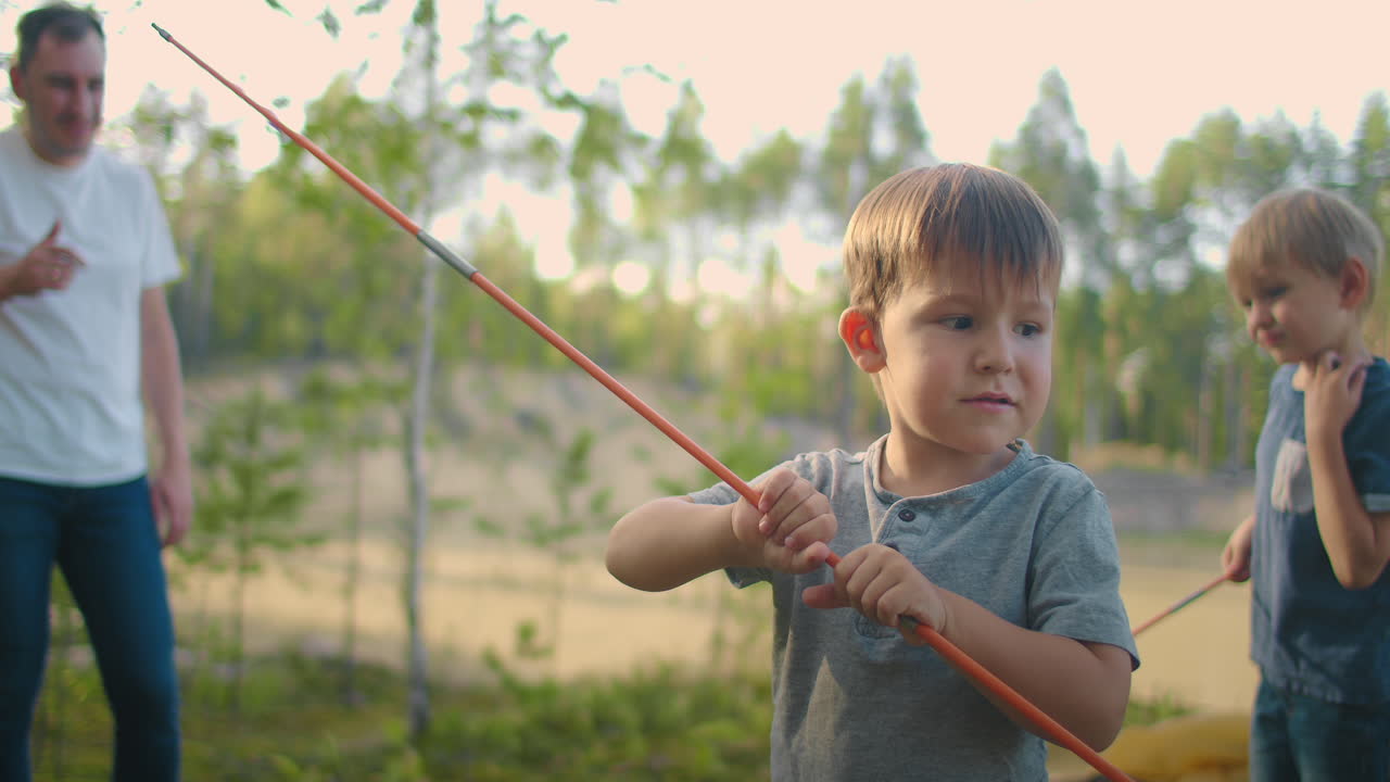 Barna sammen med faren sin setter opp et telt for natten og camper i skogen under reisen. En mann og to barn på 3-5 år sammen på fottur setter opp et telt i sakte film.