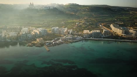 drone shot flying towards mellieha bay from a distance on a heavily misty morning in malta with mellieha church on hill in background